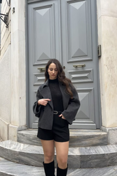 a lady in a black knit top, a grey wool jacket and a pair of black shorts